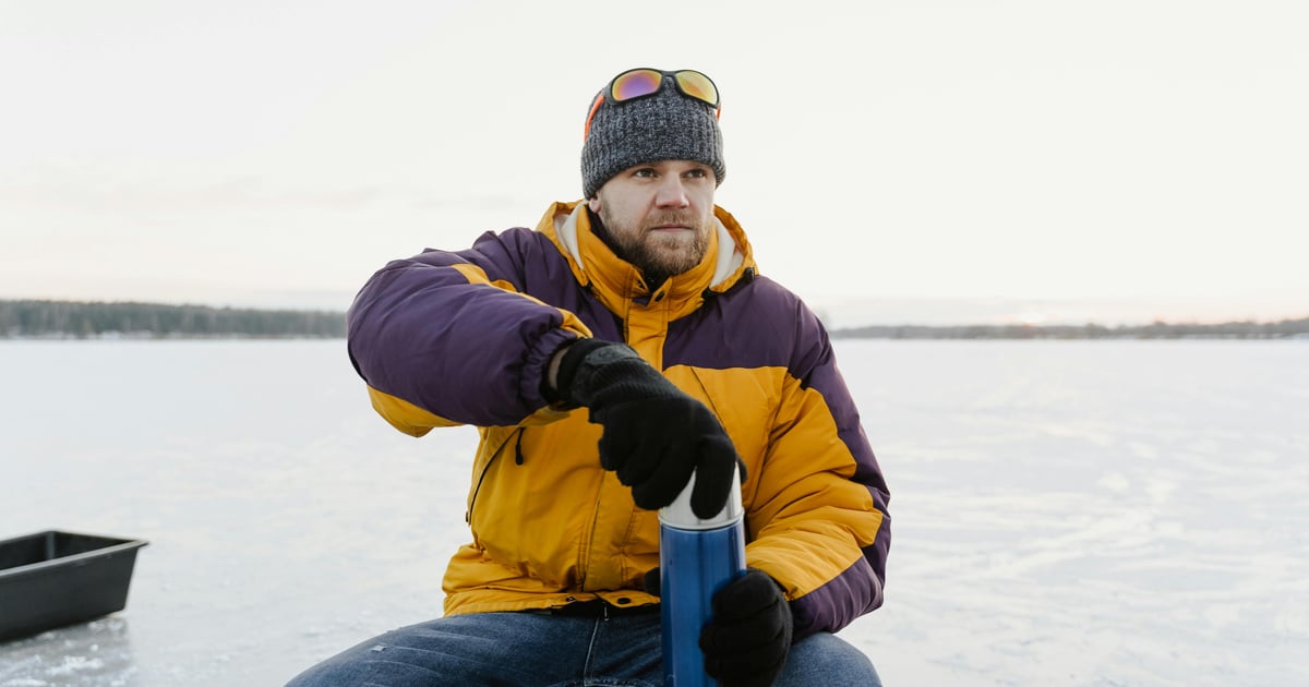A man in colorful winter clothing and beanie holding a tumbler on a snowy day.