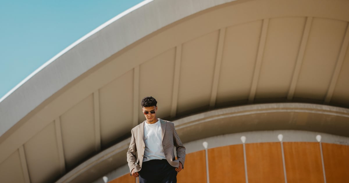 Man in stylish attire standing in front of Berlin's iconic architecture on a sunny day.