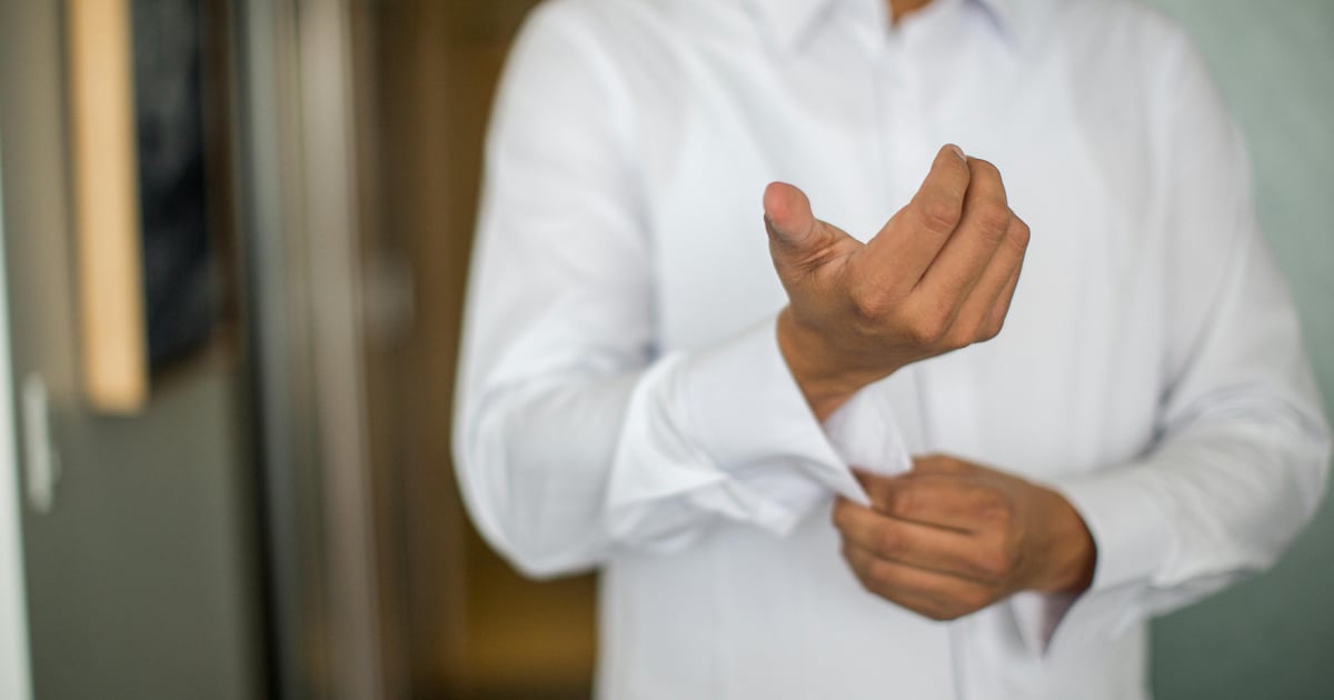 Close-up of a man adjusting his shirt cuffs, focusing on a white long-sleeve shirt indoors.