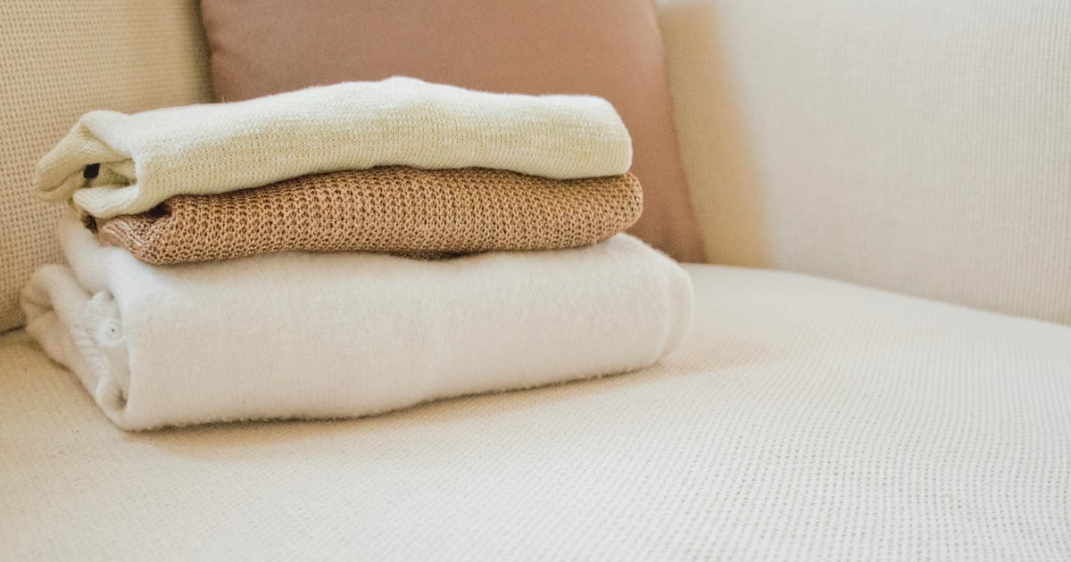Soft folded sweaters in warm tones on a cozy cream sofa, showcasing home comfort and style.