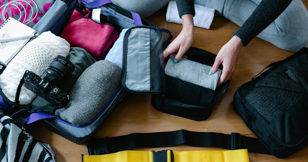 A woman arranging clothes and accessories into a suitcase, preparing for travel.